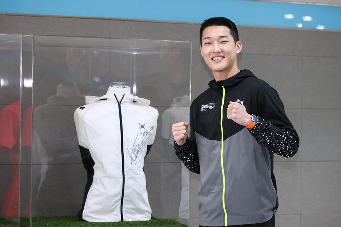 우상혁 선수가 자신이 지난 대회 때 착용했던 유니폼 전시대 앞 기념 촬영을 하고 있다.