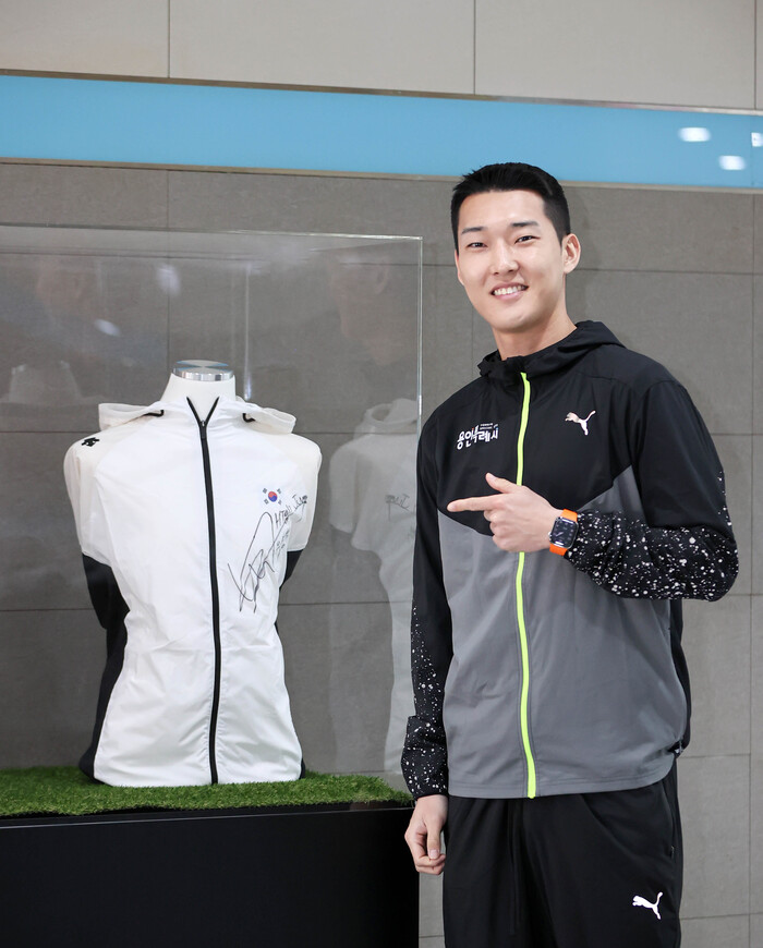 우상혁 선수가 자신이 지난 대회 때 착용했던 유니폼 전시대 앞 기념 촬영을 하고 있다.